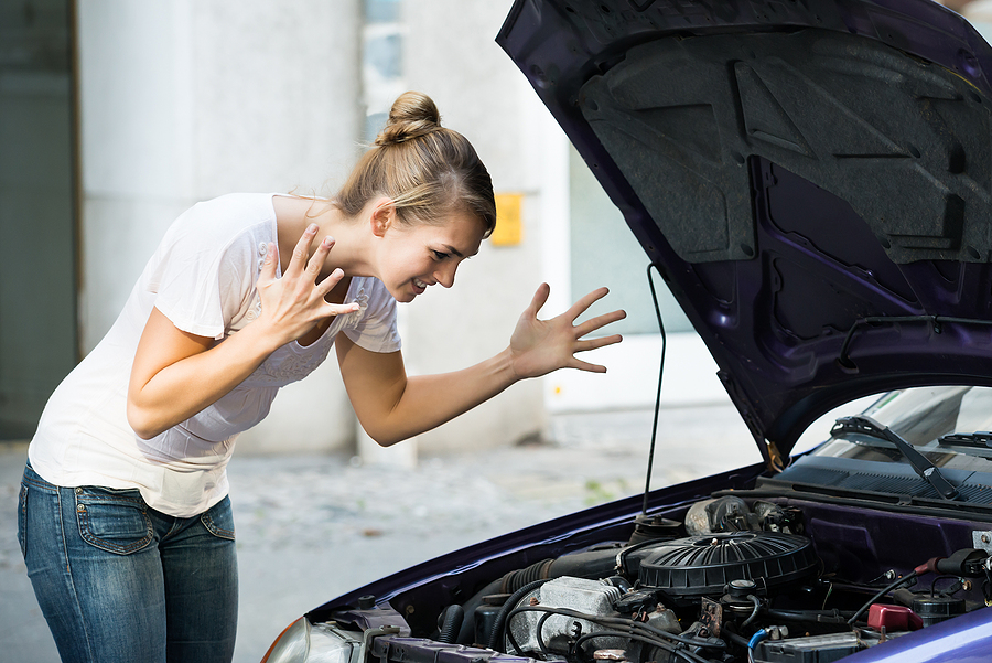 Frustrated young woman looking at broken down car engine on street